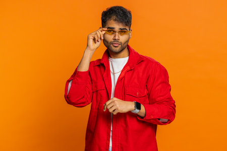Stylish man wearing sunglasses, charming smile, feels happy and successful. Young guy celebrating success victory, win, achievement isolated on orange background indoorsの写真素材