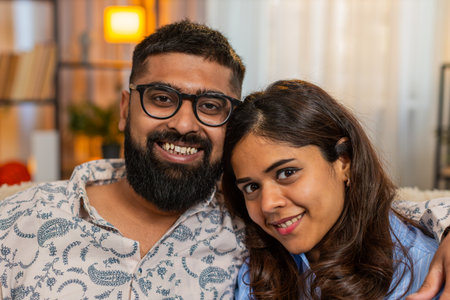 Portrait of Indian couple man and woman at home, happy looking at camera and sharing peaceful...