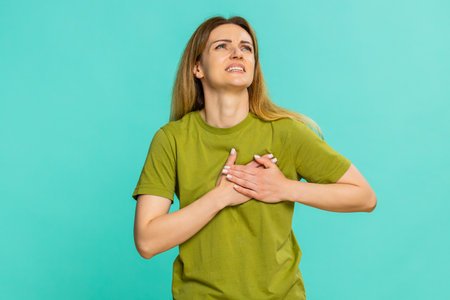 Middle-aged woman sighs and gently places hand on chest, expressing emotional exhaustion, sadness or...