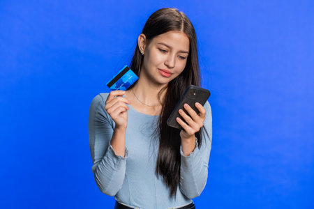 Happy young woman using credit card and smartphone while transferring spending money, purchases...