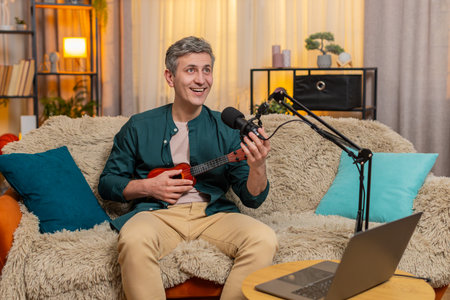 Young man blogger at home joyfully plays ukulele on sofa, singing with emotion and fun energy....