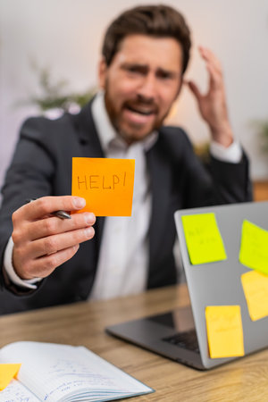 Middle-aged businessman at home office looks at laptop full of stickers for tasks and feels...