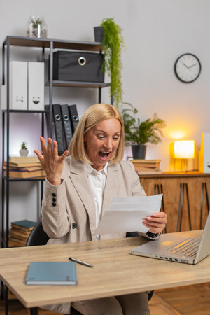 Happy Caucasian mature businesswoman open envelope letter, reading it. Career growth advance promotion, bank loan approval, successful admission to monetary award, long-awaited invitation great news.の写真素材