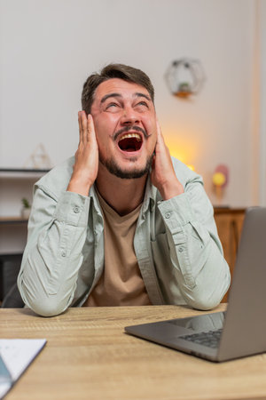 Caucasian young man freelancer shouting trying not to hear the loud noise from neighbor apartment in...
