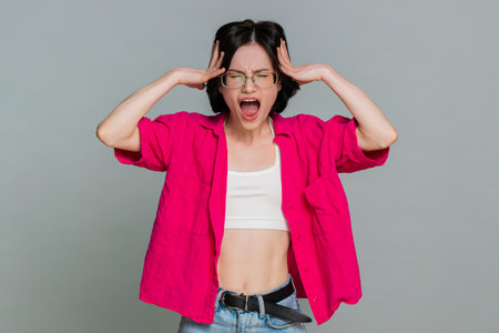 Young woman screams desperately and spreads arms aggressively, showing emotional breakdown, anger and deep frustration. Girl clearly expresses intense rage strong emotions, isolated on gray backgroundの写真素材