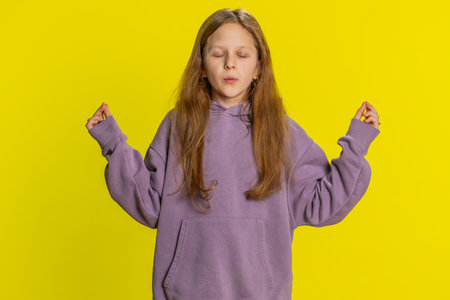 Concentrated happy preteen child girl kid meditating breathes deeply with mudra yoga gesture, eyes closed, peaceful mind taking a break. Teen children on yellow backgroundの写真素材