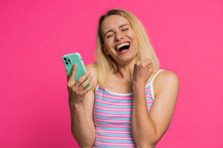 Happy excited Caucasian young woman girl use smartphone typing browsing shouting say wow yes found out great big win good news lottery goal achievement celebrating success, winning play game on pinkの写真素材
