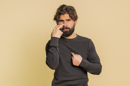 Young confident man pointing at his eyes and camera, show I am watching you gesture. Handsome bearded guy isolated alone on beige studio background.の写真素材