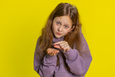 Portrait of preteen child girl kid showing a little bit gesture with sceptic smile showing minimum sign measuring small size. Children on yellow backgroundの写真素材