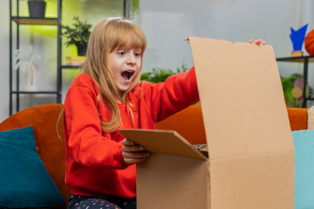 Happy amazed young child girl unpacking delivery parcel. Smiling satisfied teenager kid shopper,...