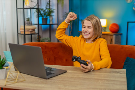 Caucasian teenager boy playing a football sports simulator on laptop at home. Child winner using a...
