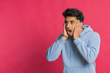 Excited amazed winner man raising hands in surprise looking at camera with big eyes, shocked by sudden victory celebrating success achievement good news. Guy on red backgroundの写真素材