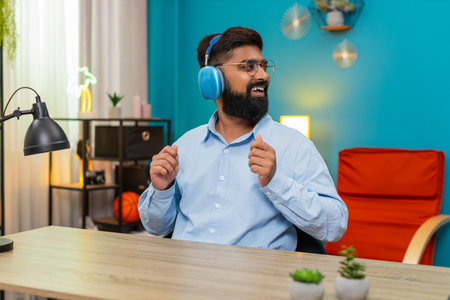 Man at home sits happy expression wearing headphones sways gently dancing enjoying calm soft music. Guy at desk keeps rhythm smiles feels peaceful mood savoring melody moments deep.の写真素材