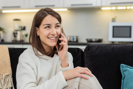 Young woman at home speaks on phone enjoys chat laughs listens and shares news in warm tone....
