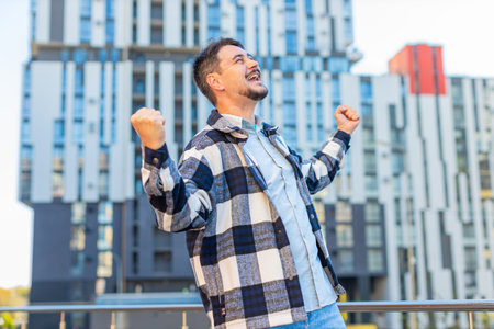 Caucasian mature man looking surprised, shocked by sudden victory, celebrating game winning, lottery goal achievement, good success news outdoors. Excited guy clenching fists on downtown city street.の写真素材