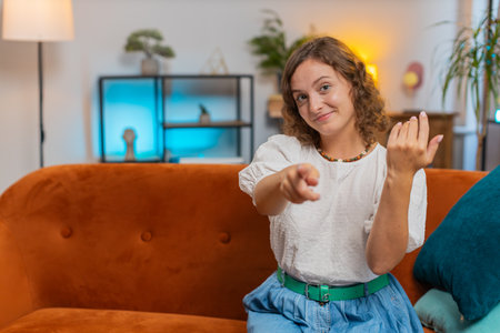 Young woman smiling excitedly and pointing to camera, choosing lucky winner, indicating to awesome you, inviting, approve. Portrait of girl at home living room sitting on couch. Lifestyles.の写真素材