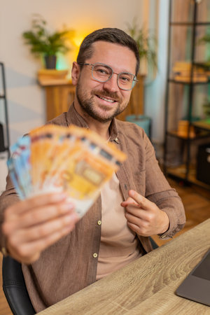 Young businessman freelancer holding fan of cash money euro banknotes, pointing and showing thumbs...