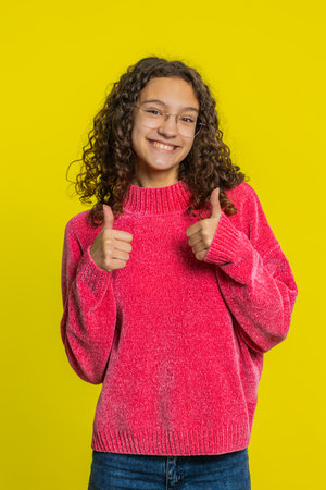 Like. Caucasian girl raises thumbs up agrees with something gives positive reply recommends advertisement likes good idea feedback celebrating success victory. Teen child isolated on yellow backgroundの写真素材