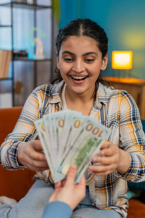 Young woman experiencing sudden happiness, joyfully celebrating on sofa receiving plenty of cash. Girl sincerely delighted, smiling widely, enthusiastically showing victory winの写真素材