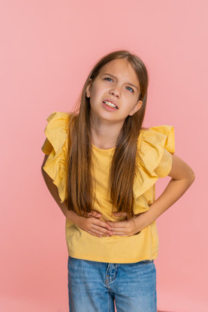 Young child girl holds her stomach with frightened expression, showing that something hurts and feeling unwell. School kid isolated on pink background showing pain and reaction related to health issueの写真素材