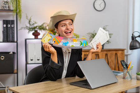 Young businesswoman at home office completes ticket purchase on laptop smiling after payment approval. Freelancer girl at table closes laptop wears inflatable ring dreaming about upcoming vacation funの写真素材