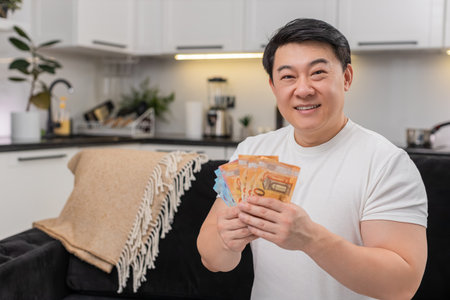 Asian man at home counts cash euros smiles makes money sign plans purchase and thinks about savings...