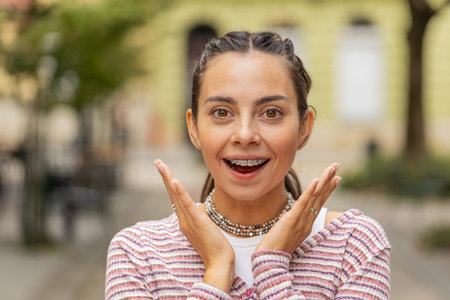 Portrait of excited Caucasian young woman tourist with braces on teeth walking on urban city street daytime outdoors. Girl expresses amazement, wow emotion, positive good mood enjoying sightseeingの写真素材