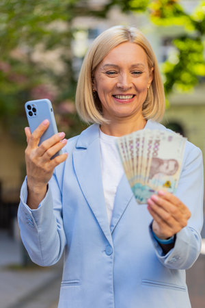 Mature businesswoman standing on city street showing earnings winning at betting cash money with...