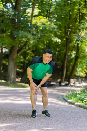 Runner athlete with muscle pain in sunny park. Man massaging stretching, injury while jogging...