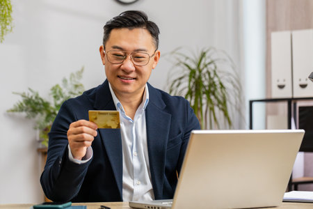 Chinese businessman programmer software developer working making online purchase payment shopping with credit bank card and use laptop at home office desk with laptop. Asian freelancer business manの写真素材
