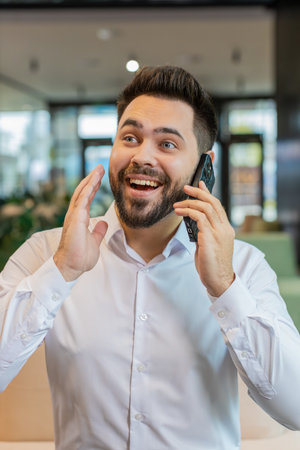 Smiling young businessman in formal shirt working, having mobile phone talk in modern office lobby. Professional manager man guy holding smartphone using messenger chat apps. Employment, occupation.の写真素材