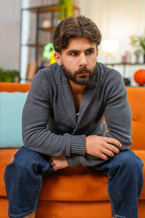 Man at home bends forward holds head in hands strong fatigue slow breath eyes down seeks rest. Guy on sofa sits still rubs temples tries to calm mind seeks relief from stress and pain.の写真素材