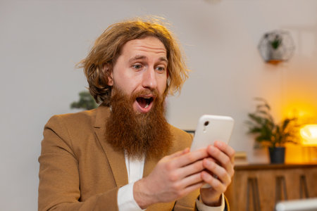 Happy amazed young Caucasian businessman working on smartphone shocked by sudden victory, game...