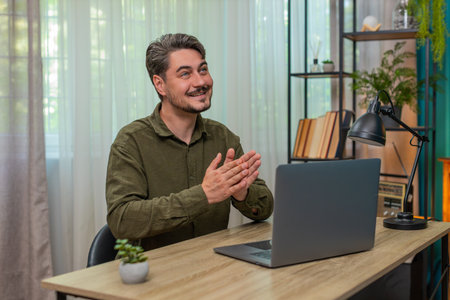 Middle-aged man at home reviews laptop report claps hands pleased winning big deal profit achieved....