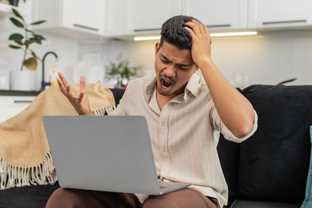 Indian man at home reads work rejection on laptop holds head takes deep breath, game fail makes...