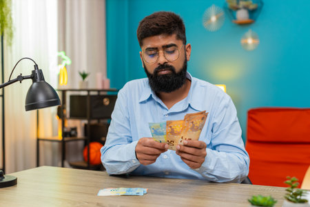 Man at home counts cash banknotes stacking piles feels wealthy after salary profit winnings. Arabian...