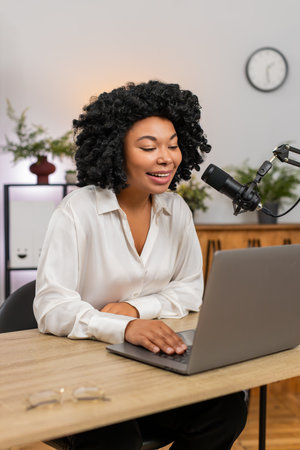 African American businesswoman at home office records vlog with microphone gestures beside laptop....