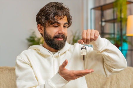 Happy man real estate agent lifting hand showing the keys of new home house apartment, buying or...