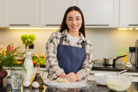 Young woman kneads elastic dough on floured board mixing eggs milk and oil for homemade bread. Girl...