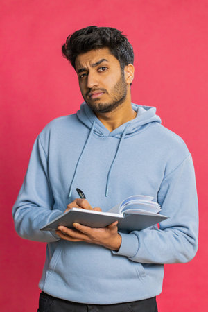Thoughtful journalist young man making notes, writing down thoughts with pen into notepad notebook diary, to do list, good idea inspiration. Guy isolated on red backgroundの写真素材