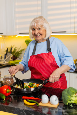 Senior old woman cooking vegetables in home kitchen smelling fresh food with satisfaction for healthy diet. Elderly grandmother preparing dinner in pan focusing on nutrition health weightloss recipe.の写真素材