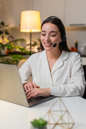 Young woman at night home works as call center agent with headset answers support call and logs...