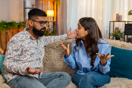 Couple man and woman sitting on home sofa, having emotional discussion and small disagreement with expressive gestures. Young family involved in everyday argument without conflict or aggressionの写真素材