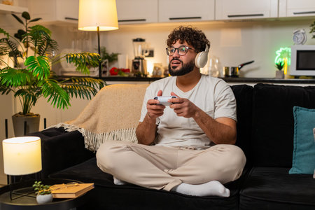 Man at home plays on game console holds joystick leans forward enjoys play sees level score high....