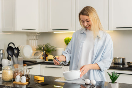 Middle-aged woman whisking eggs in bowl in kitchen making omelet batter for healthy fit meal. Young...