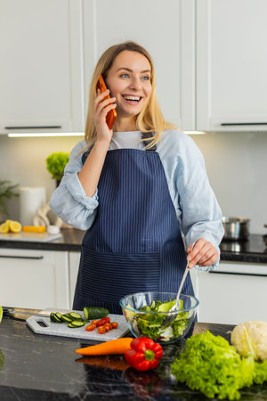 Middle-aged woman talks on smartphone while mixing vegetable salad for keto diet in home kitchen....