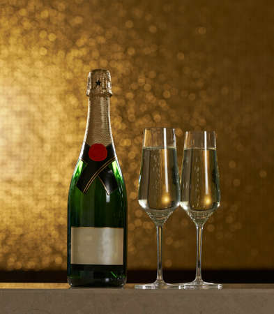 A bottle of champagne with two glasses on a golden backgroundの写真素材