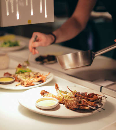 Chef in a kitchen cooking lobsters and grilled shrimps, side view. The chef cooks shrimps for salad, and sprinkles on a skillet. Freezes in motion.の写真素材