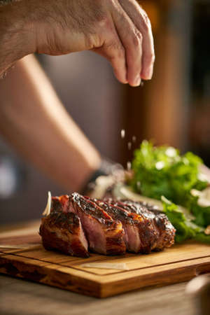 Chef's hand putting salt on a steak, cut meat on a wooden board.の写真素材