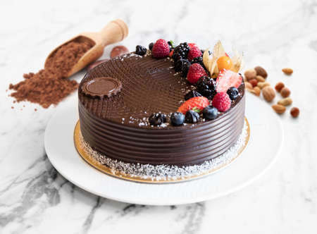 Dessert chocolate cake with berries on a table with almonds and coca powder, side view. whole chocolate cake with berries on top.の写真素材